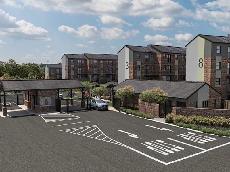 A modern townhouse complex entrance featuring a secure gatehouse, paved driveway, and multi-story residential blocks with brick and plaster finishes.