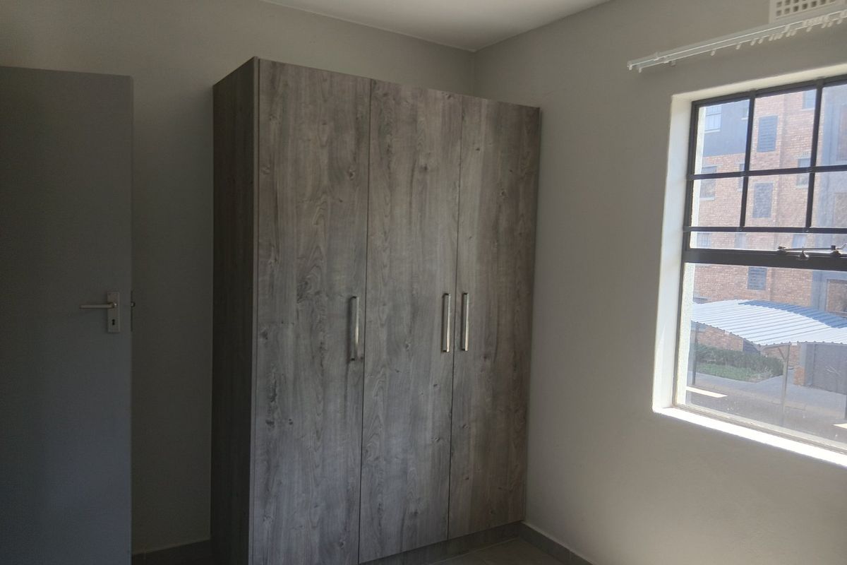 A clean, empty bedroom featuring a modern wood-finish built-in wardrobe, tiled flooring, and a window with security bars.