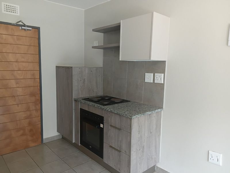 Compact kitchen area featuring modern grey laminate cabinetry, granite countertops, a built-in oven, electric hob, and neutral tiled flooring.