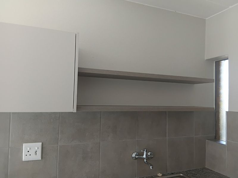 A clean kitchen area featuring modern wall-mounted cabinetry, open shelving, and a tiled splashback with a wall-mounted tap.