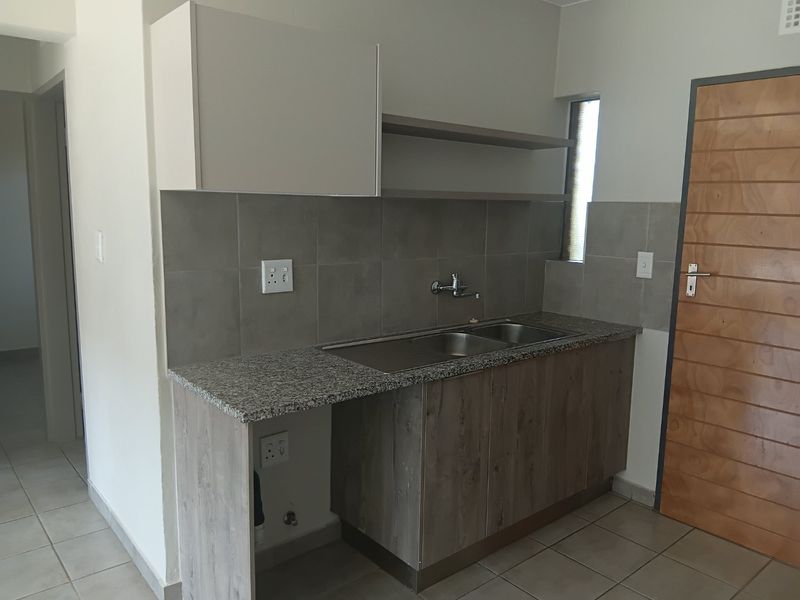 A functional scullery area featuring a double bowl stainless steel sink, granite countertops, laminate cabinetry, and tiled splashbacks with dedicated plumbing connections.