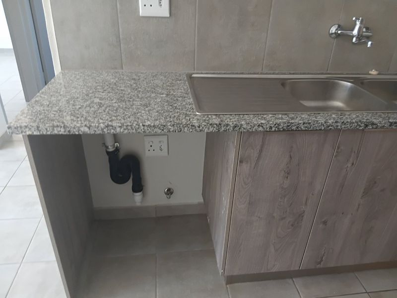 A functional kitchen area featuring granite countertops, a stainless steel double sink, and modern wood-look cabinetry with dedicated plumbing connections for appliances.