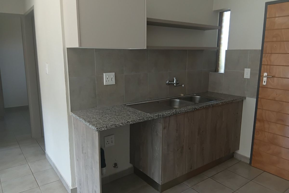 A clean and functional kitchen area featuring granite countertops, a double stainless steel sink, tiled splashbacks, and modern wood-finish cabinetry.