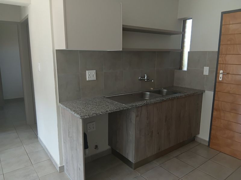 A clean and functional kitchen area featuring granite countertops, a double stainless steel sink, tiled splashbacks, and modern wood-finish cabinetry.