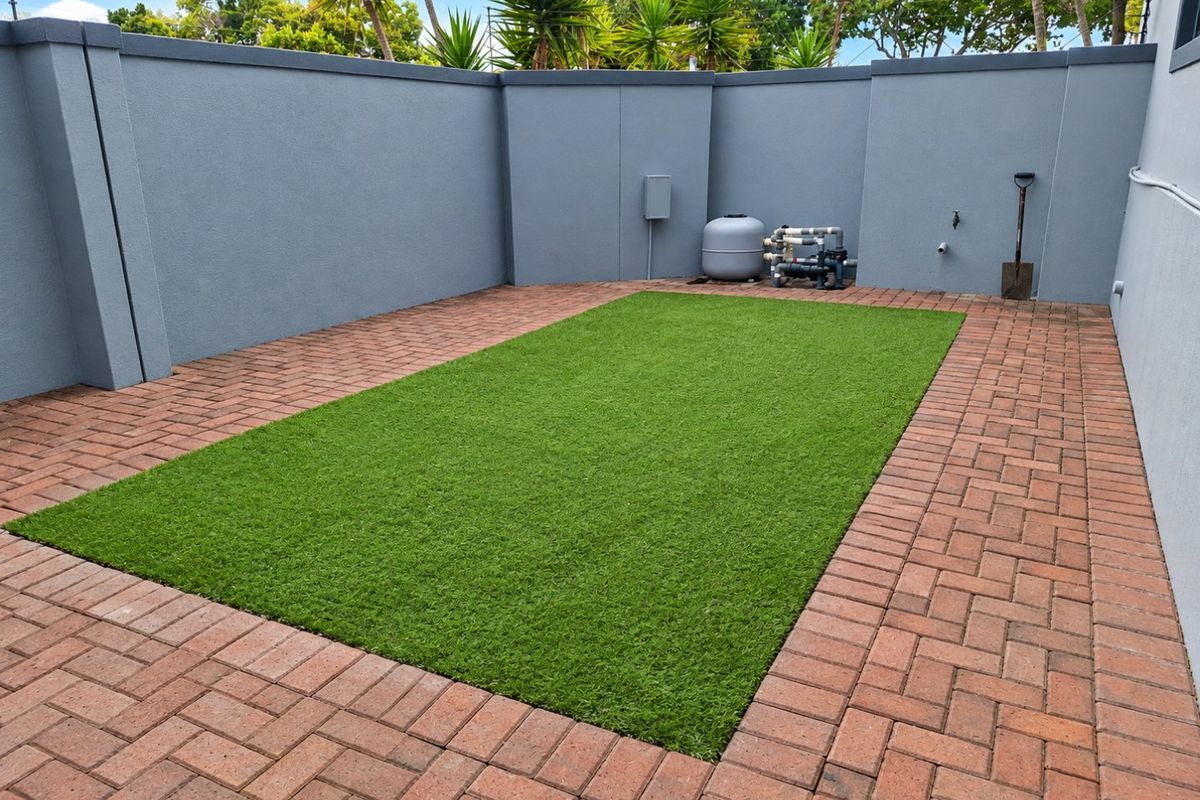 A well-maintained rear courtyard featuring artificial turf, brick paving, and a perimeter boundary wall with an integrated pool filtration system.