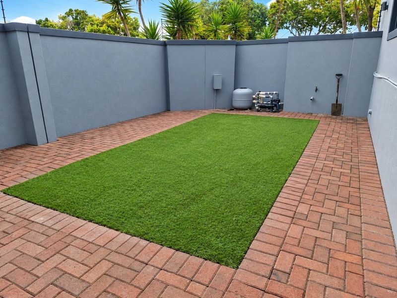A well-maintained rear courtyard featuring artificial turf, brick paving, and a perimeter boundary wall with an integrated pool filtration system.