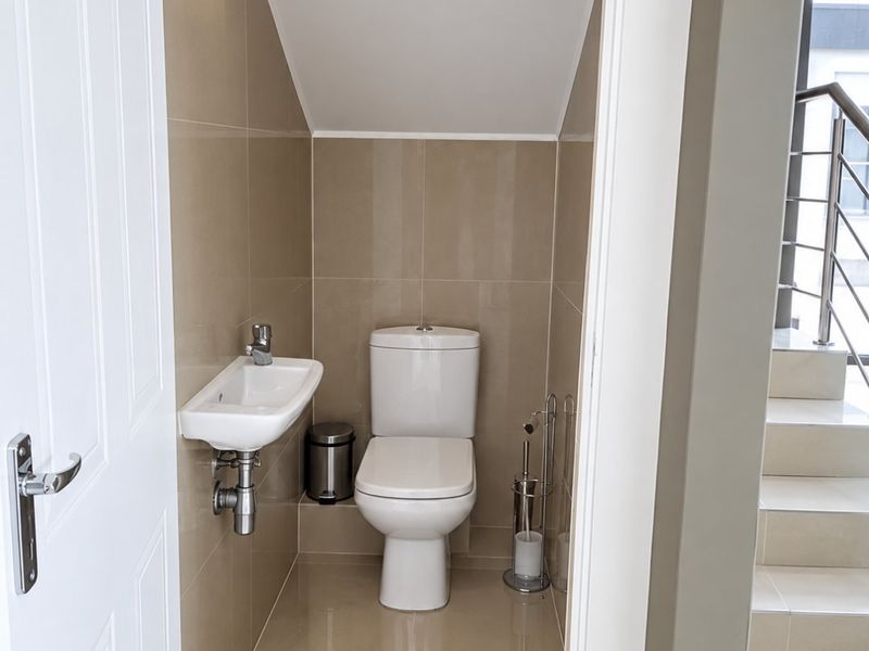 A compact guest bathroom featuring modern tiled finishes, a wall-mounted basin, and a toilet, conveniently located under the staircase.