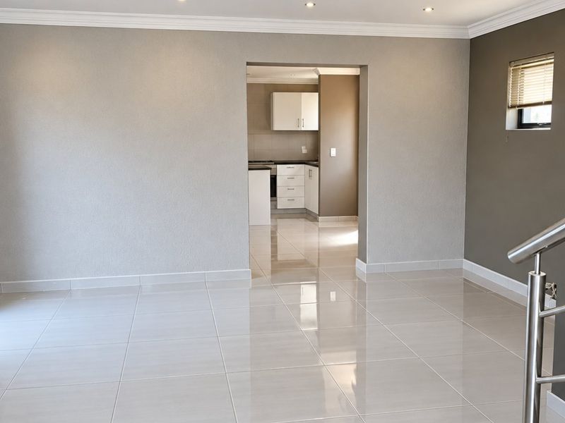 Spacious open-plan living area featuring polished porcelain tiles, recessed downlighting, and a modern stainless steel balustrade, leading into a clean, functional kitchen space.