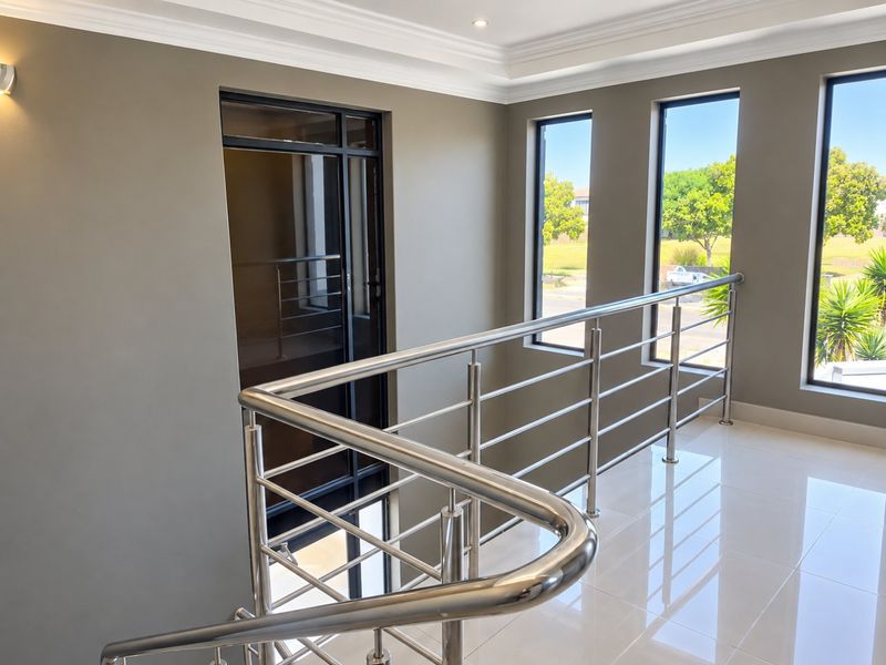 A bright, modern landing area featuring polished porcelain floor tiles, a sleek stainless steel balustrade, and large windows providing ample natural light.