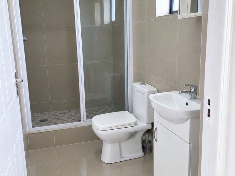 A clean and modern bathroom featuring a walk-in shower with sliding glass doors, a white vanity basin, and neutral floor-to-ceiling tiling.