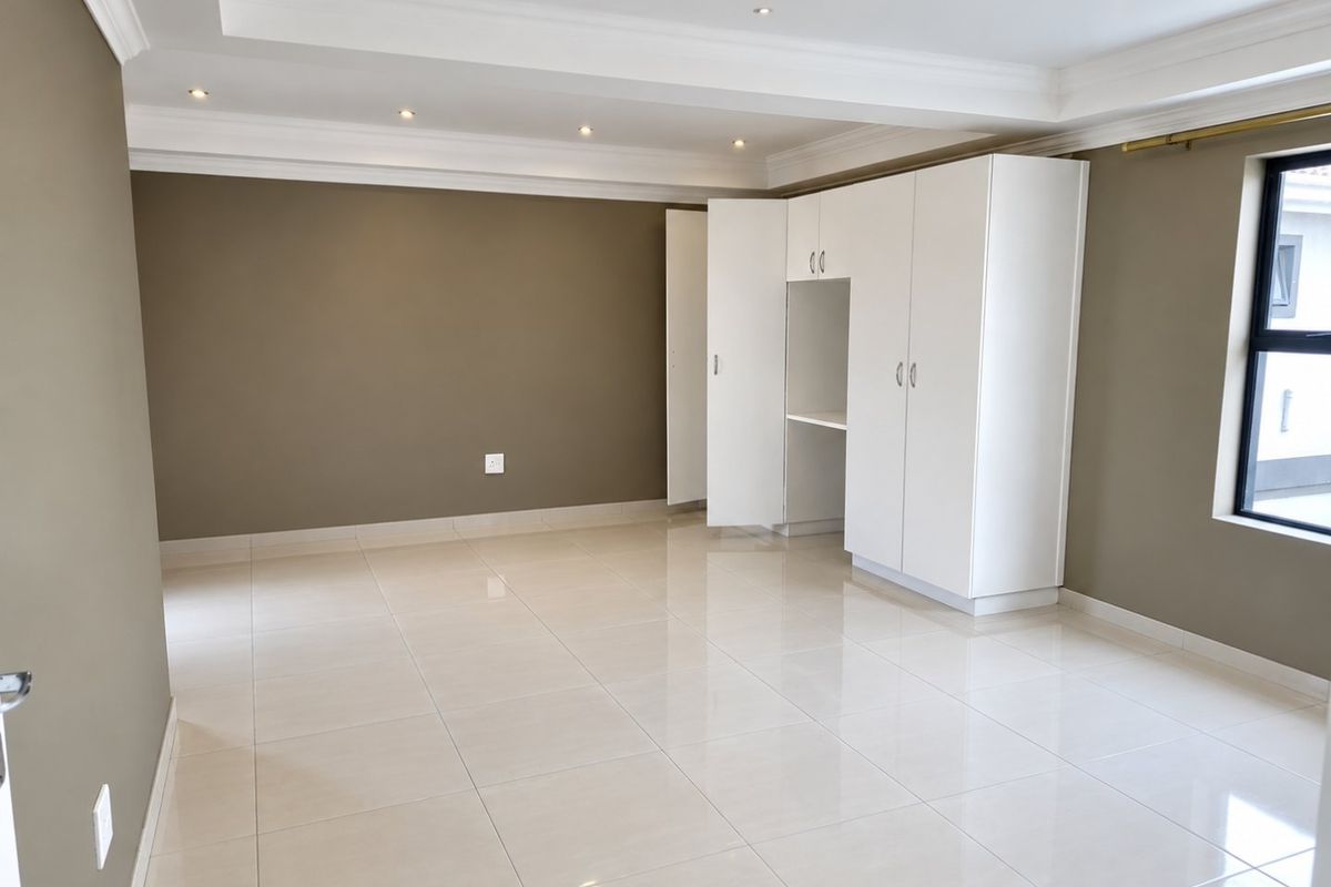 A spacious, empty bedroom featuring neutral wall tones, polished tiled flooring, recessed ceiling lights, and ample built-in cupboard storage.