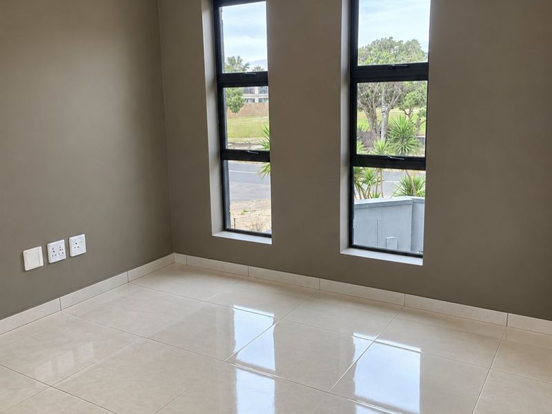 A bright, empty bedroom featuring polished tiled flooring, recessed ceiling lighting with decorative molding, and dual windows with a curtain rod.