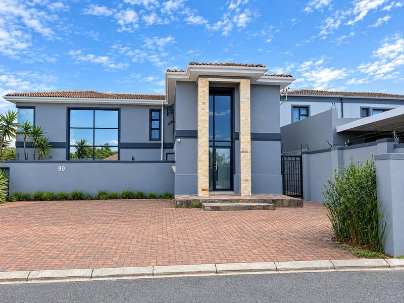 Modern double-story apartment facade featuring stone cladding, large glass entrance, paved driveway, and secure perimeter wall with electric fencing.