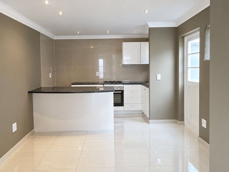 A clean, modern kitchen featuring white cabinetry, dark granite countertops, gas hob, built-in oven, and polished tiled flooring with direct exterior access.