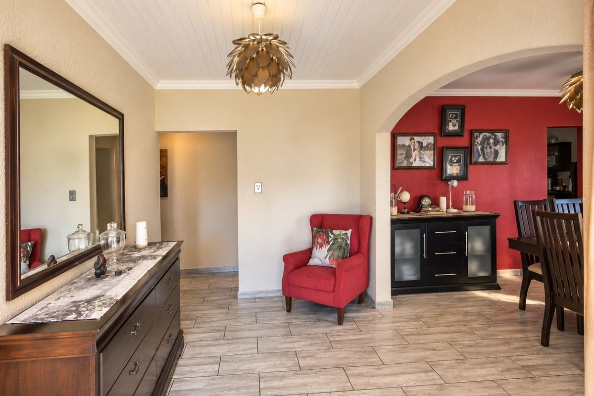 A well-maintained living area featuring tiled flooring, a distinctive tongue and groove ceiling, and an elegant archway leading to the dining space.