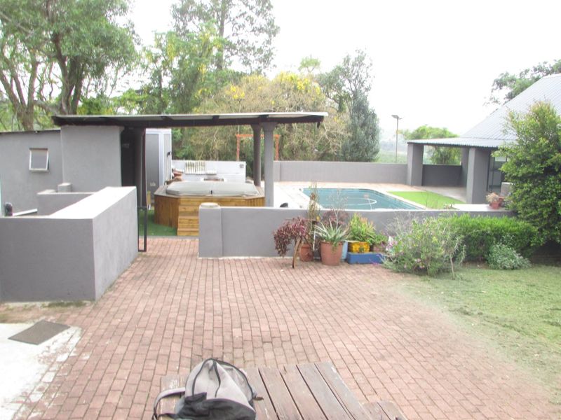 Outdoor entertainment area featuring a swimming pool, built-in jacuzzi, covered patio space, and brick paved surroundings on a farm property.