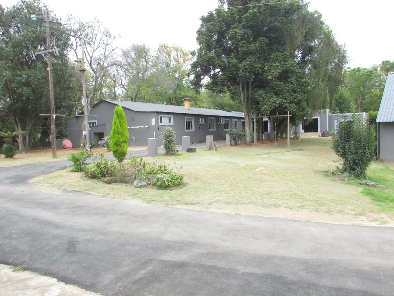 A view of the rear exterior of the farm property, featuring a paved driveway, established garden, and the main building structure.