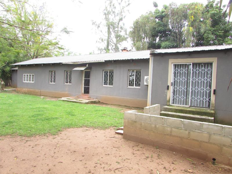 Rear view of a farm dwelling featuring a corrugated metal roof, security bars on windows, and an unfinished cinder block wall section.