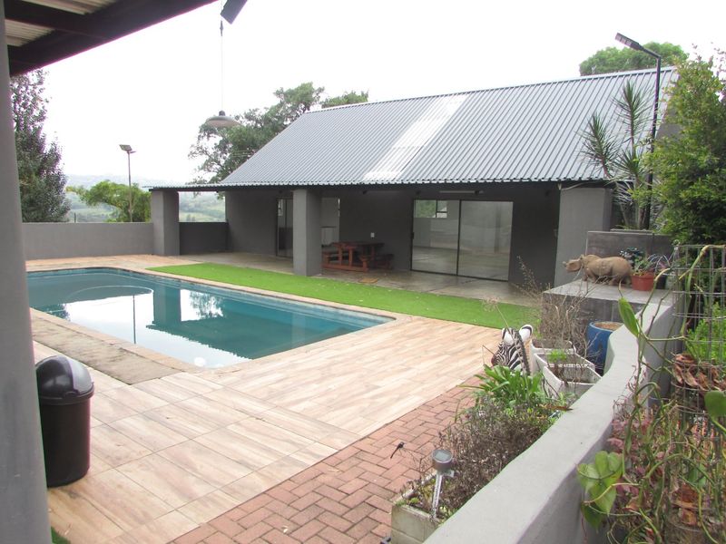Outdoor pool area featuring a tiled deck, brick paving, and a covered patio space with sliding glass doors under a corrugated metal roof.