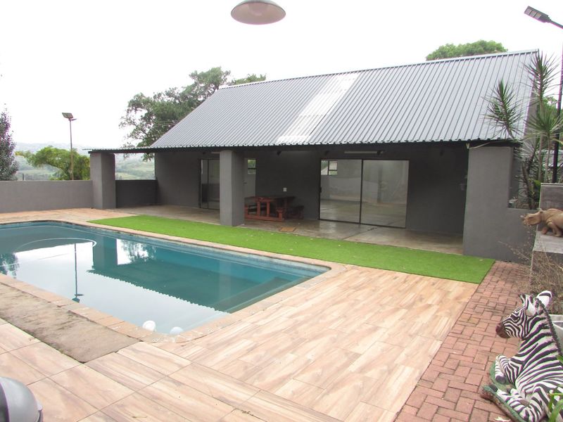 Outdoor pool area featuring a swimming pool, covered patio with sliding glass doors, artificial turf, and a combination of tiled and brick paved decking.