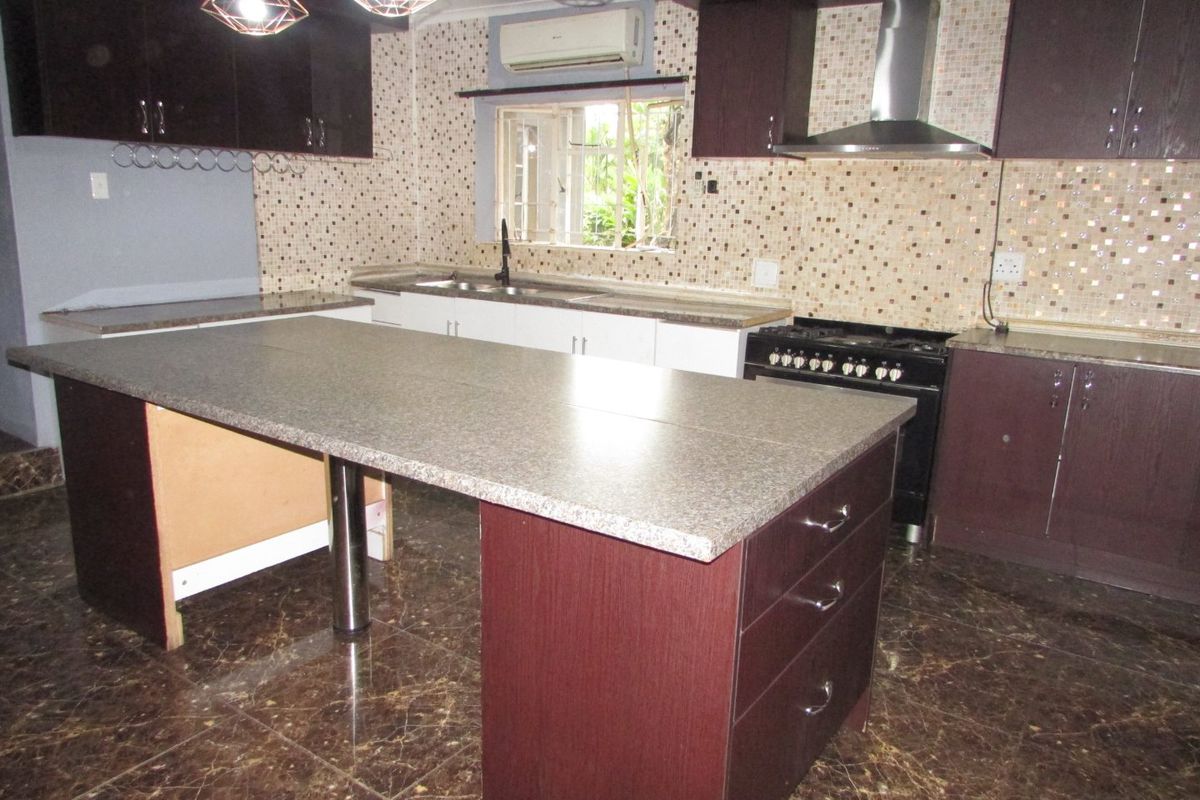 Spacious kitchen featuring dark wood cabinetry, granite countertops, a central island, gas stove with extractor, and mosaic tile backsplash.