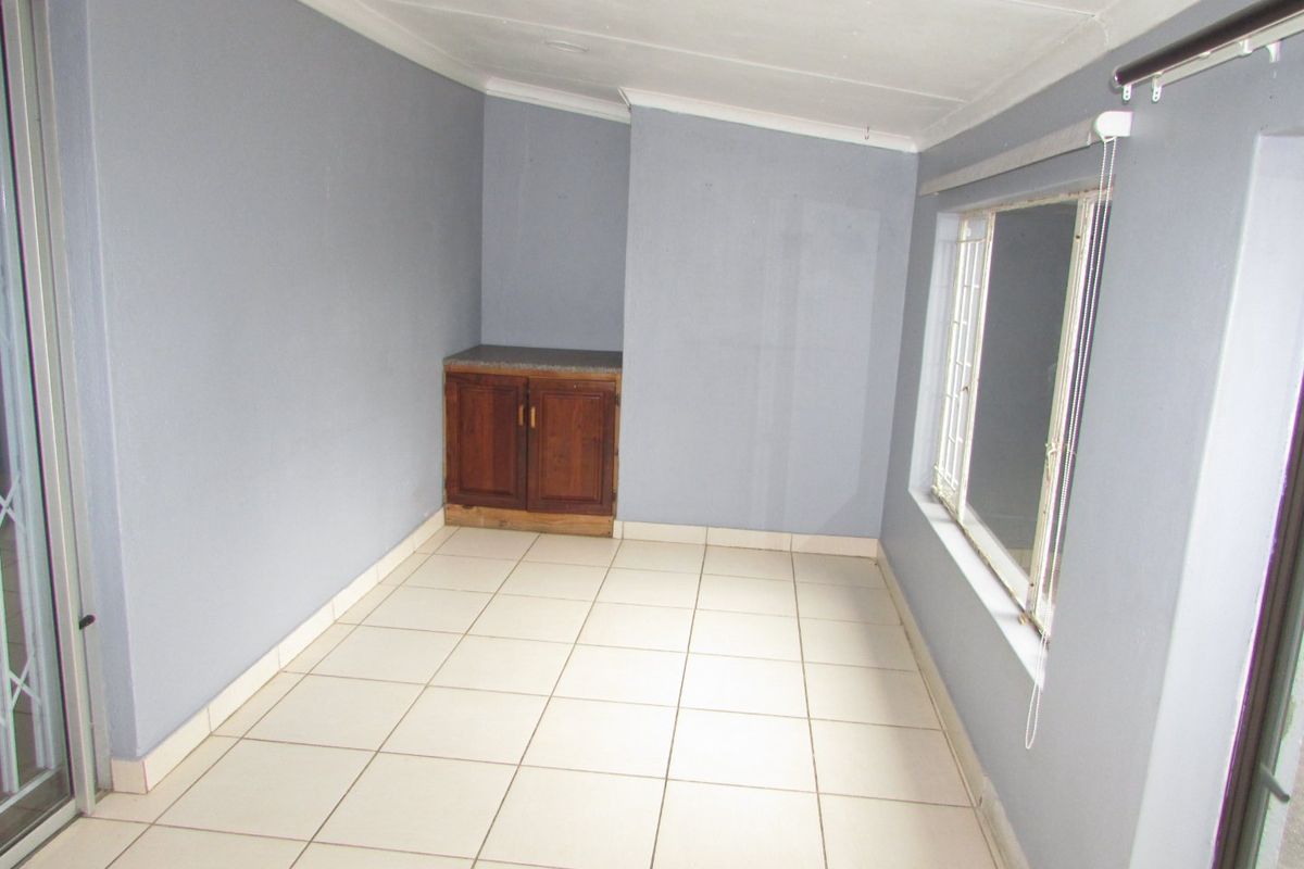 An empty living area featuring tiled flooring, a built-in wooden cabinet, and large windows with security bars.