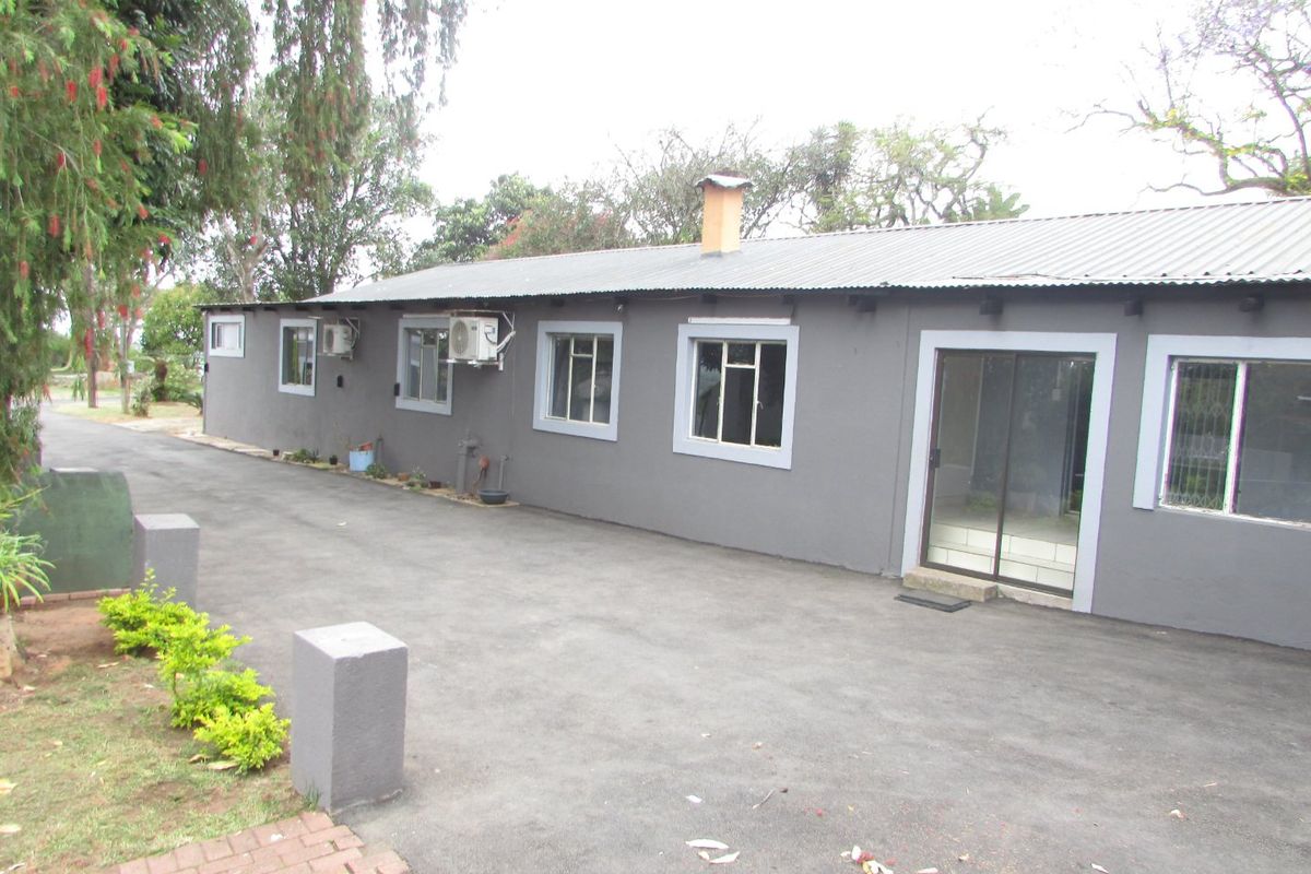 Rear exterior view of the farm building featuring a corrugated metal roof, chimney, sliding glass door, and an adjacent asphalt driveway.
