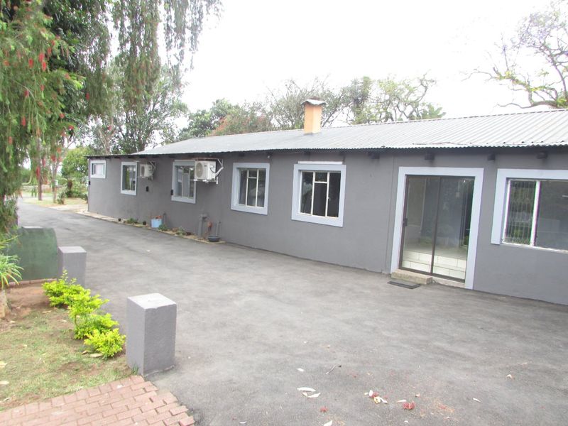 Rear exterior view of the farm building featuring a corrugated metal roof, chimney, sliding glass door, and an adjacent asphalt driveway.