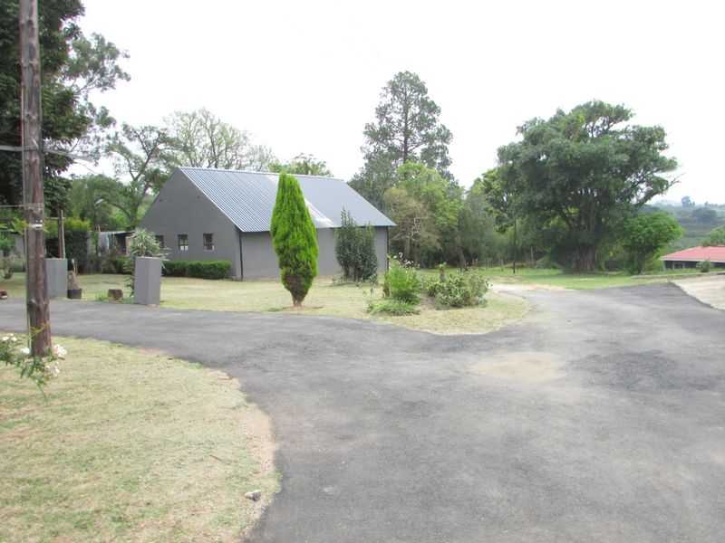 A view of the property entrance featuring an asphalt driveway leading towards a farmhouse with a metal roof and landscaped garden area.