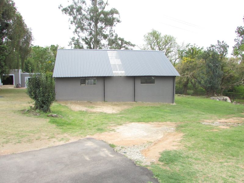 A detached outbuilding featuring a grey plastered exterior and a corrugated metal roof with a central skylight, situated on a rural farm property.