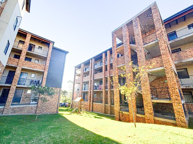 Exterior view of a multi-story apartment complex featuring face brick facades, private balconies with metal railings, and a shared communal garden area.