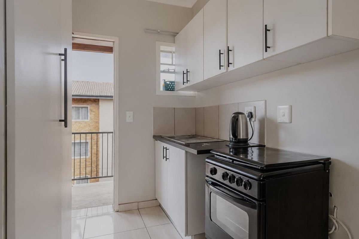 Compact kitchen featuring white cabinetry, tiled backsplash, and a freestanding stove, with direct access to an outdoor balcony area.