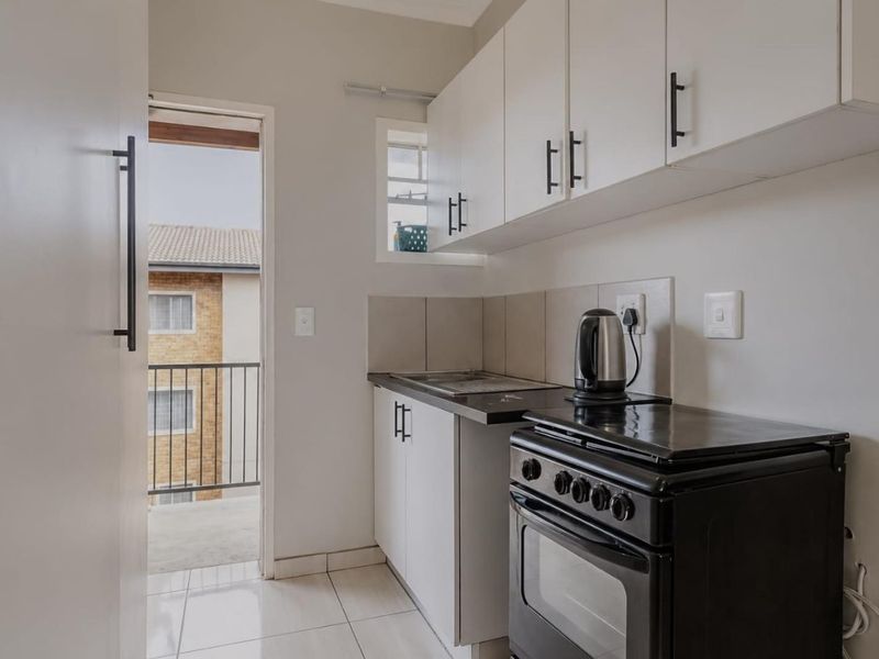 Compact kitchen featuring white cabinetry, tiled backsplash, and a freestanding stove, with direct access to an outdoor balcony area.