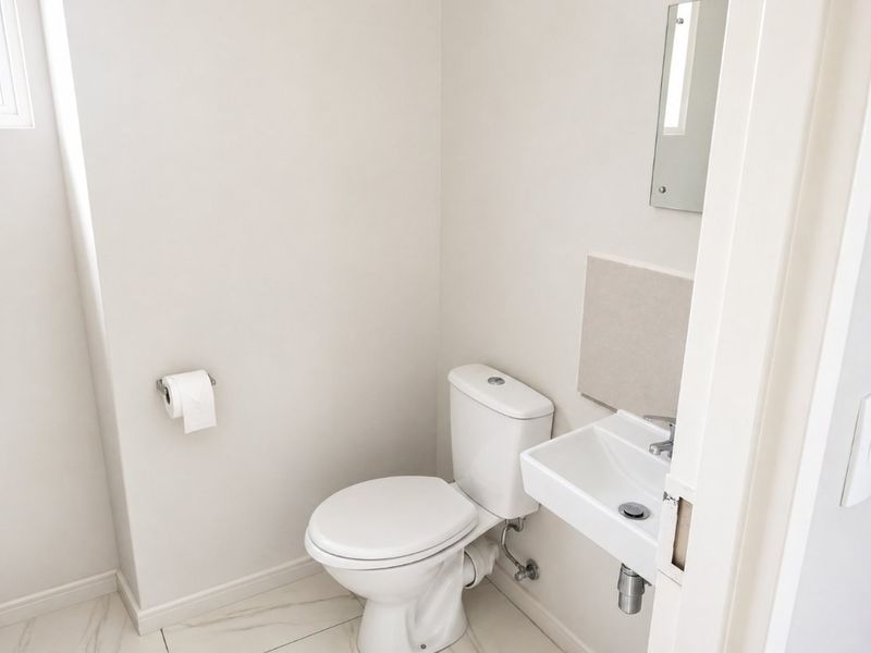 A clean and modern guest bathroom featuring a white toilet, wall-mounted basin, and neutral tiled flooring.