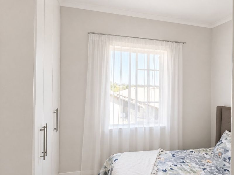 A bright bedroom featuring built-in cupboards and a window with natural light, offering a clean and neutral living space.