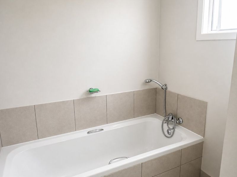 A clean and functional bathroom featuring a built-in bathtub with chrome fixtures and neutral-toned wall tiling.