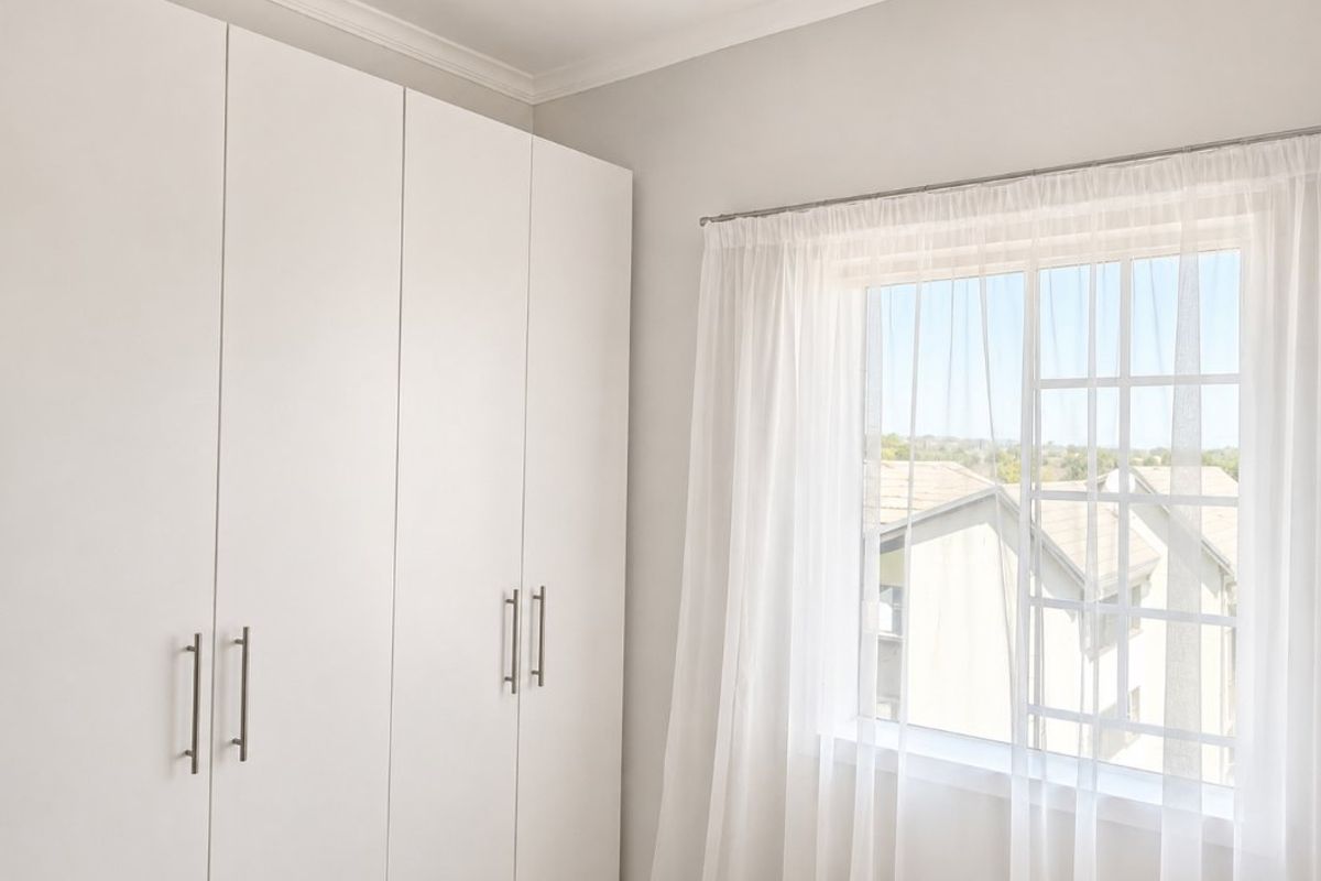 A bright bedroom featuring clean white built-in cupboards, a window with muntins, and classic cornice detailing.