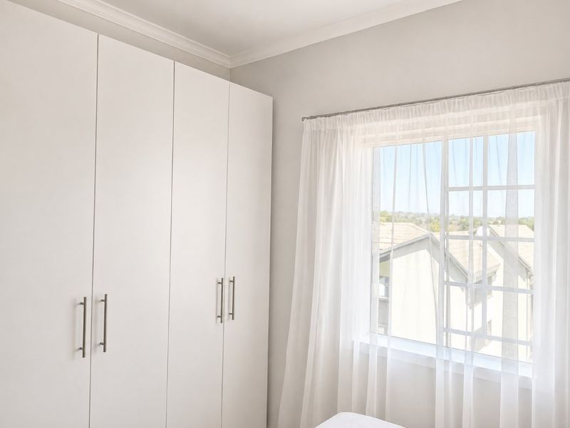 A bright bedroom featuring clean white built-in cupboards, a window with muntins, and classic cornice detailing.