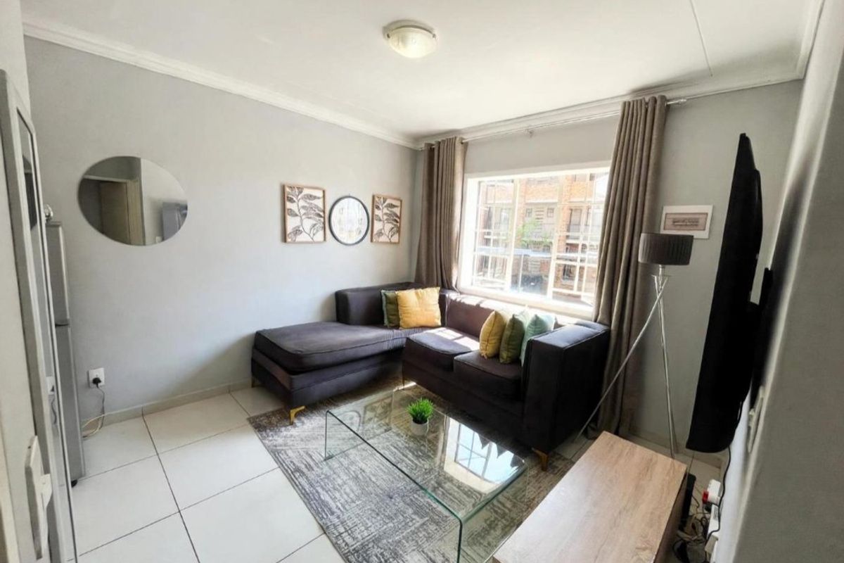 A well-lit living room featuring neutral wall tones, large windows, and clean tiled flooring, providing a comfortable and functional space.