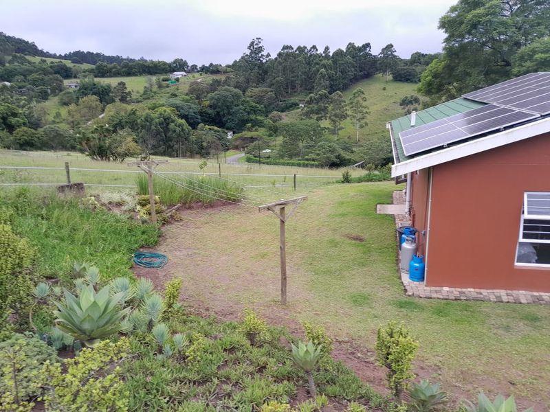 Rear exterior view of the property featuring a metal roof with installed solar panels, brick paving, and a spacious garden area overlooking rural landscape.