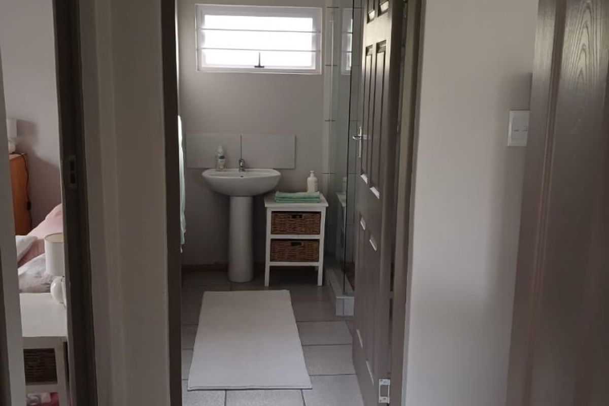 A functional bathroom featuring a pedestal basin, tiled flooring, and a shower enclosure, viewed from the adjacent hallway.