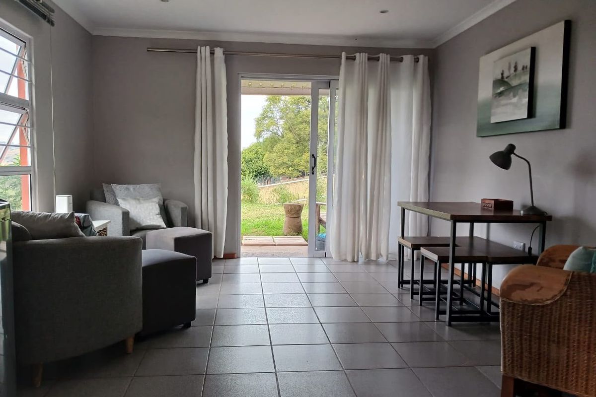 A bright living area featuring neutral tiled flooring, recessed lighting, and a sliding glass door providing direct access to the outdoor garden space.