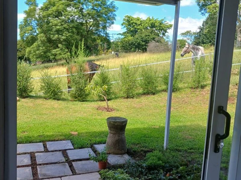 A covered patio area featuring a sliding glass door and paved walkway, overlooking a lush green garden and rural landscape.