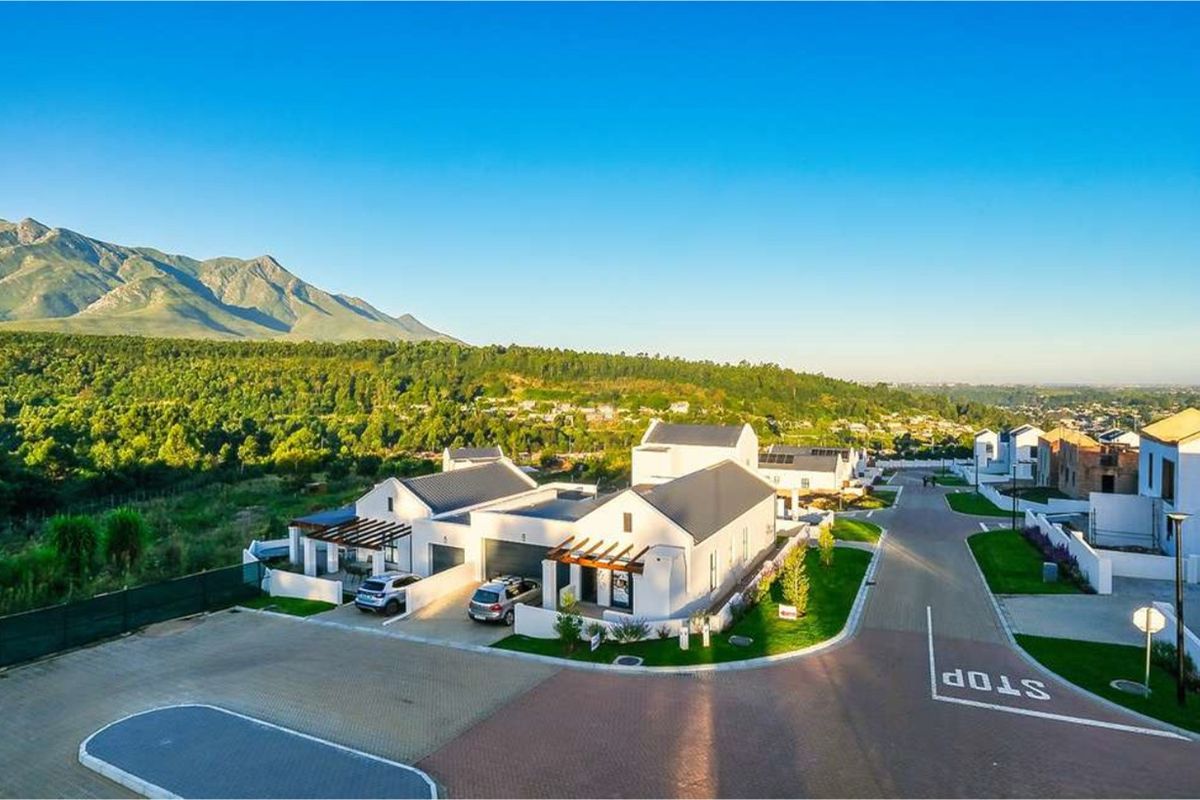 An elevated aerial view of a modern residential estate featuring contemporary homes with pitched roofs, paved driveways, and scenic mountain views.