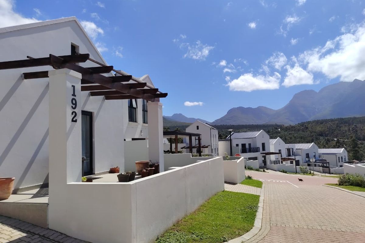 A modern residential exterior featuring a timber pergola entrance, paved driveway, and well-maintained boundary walls with scenic mountain views in the background.