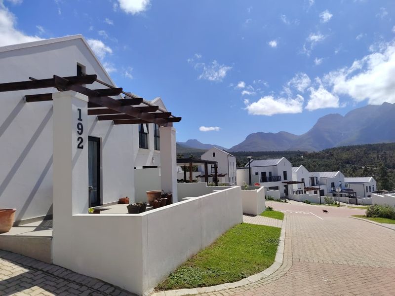 A modern residential exterior featuring a timber pergola entrance, paved driveway, and well-maintained boundary walls with scenic mountain views in the background.