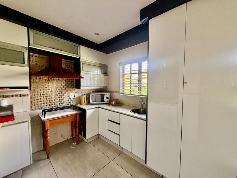 A functional kitchen featuring white cabinetry, a tiled backsplash, an extractor fan, and a stainless steel sink with tiled flooring throughout.