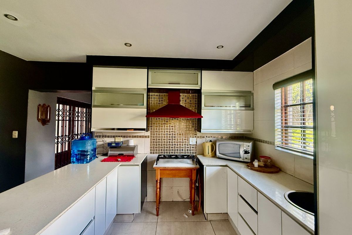 A functional kitchen featuring white cabinetry, stone countertops, a tiled backsplash, and a red extractor fan, with integrated lighting and a window for natural light.