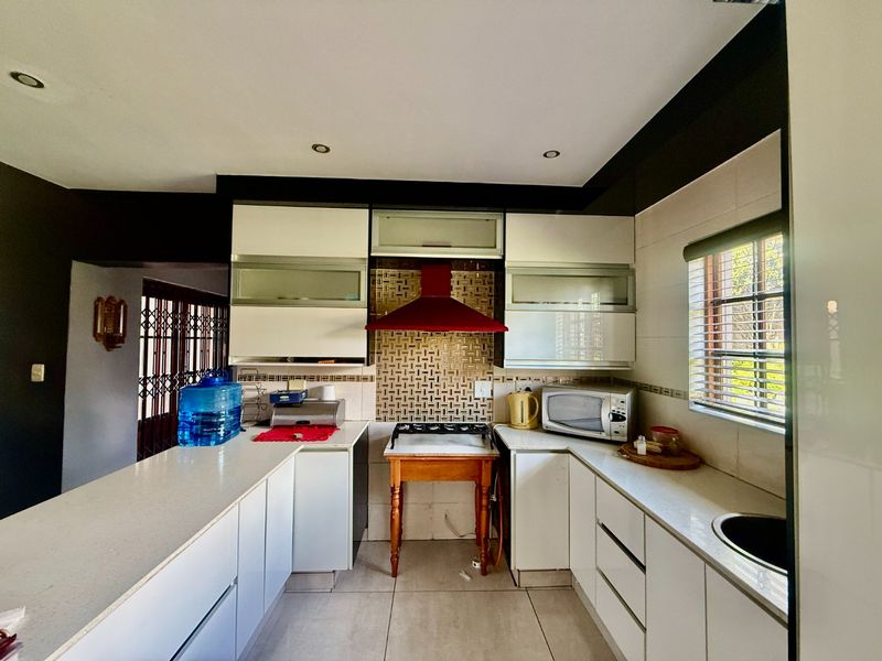 A functional kitchen featuring white cabinetry, stone countertops, a tiled backsplash, and a red extractor fan, with integrated lighting and a window for natural light.