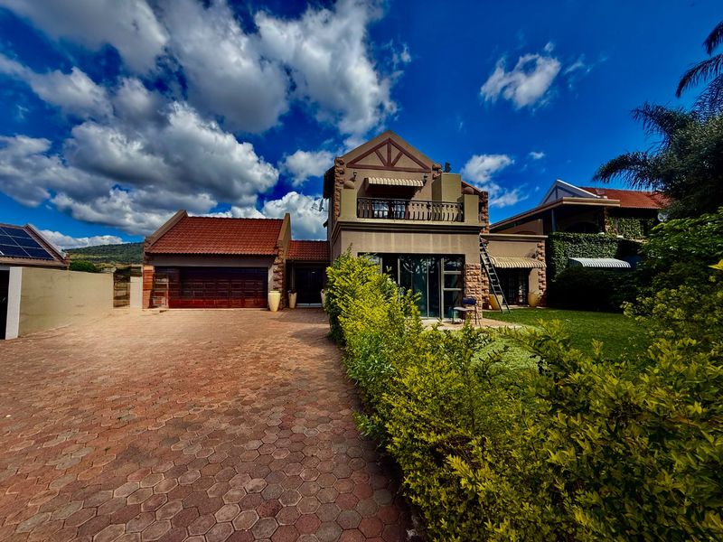 A well-maintained double-story house featuring stone cladding, a paved driveway, a double garage, and an upper-level balcony overlooking the front garden.